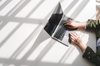 A person typing on a laptop with sunlight casting shadows onto the surface.