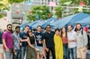 A diverse group of people smiling at an outdoor event with tents and hanging flags.
