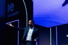 A man presenting on stage at an event with IE University branding in the background.