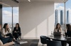 A group of women engage in a business meeting with a city skyline visible through large windows.