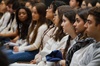 A group of young people is attentively sitting in a seminar or lecture hall.