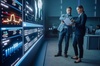 Two colleagues are discussing data on a digital display in a modern office environment.
