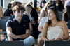 A young man and woman smiling and talking, sitting in a room filled with people.