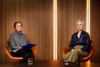 Two women seated in stylish chairs engage in conversation on a modern set.