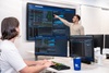 Two people working in a modern office environment with multiple monitors displaying data.