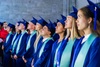 A group of graduates wearing blue caps and gowns, looking upward during a ceremony.
