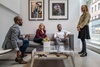 Four people, two men and two women, are having a lively conversation in a modern office lounge area.