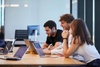 A group of young people collaborating around a table with laptops in a modern workspace.