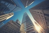 Looking up at towering skyscrapers against a clear blue sky with sunlight shining through.