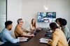 A group of people in a meeting room engaged in a virtual conference displayed on a screen.