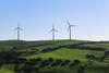 Three wind turbines stand on green hills under a clear blue sky.