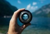 A hand holding a camera lens with a scenic view visible through it.