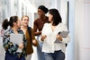 A group of four young women are walking and chatting together in a hallway.