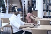Two individuals wearing virtual reality headsets are engaged in a digital experience in a library.