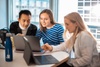 Three individuals are collaborating on laptops at a bright, modern workspace.