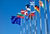 A collection of flags from various countries waving against a clear blue sky.