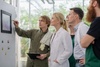 A group of professionals is discussing a display on a wall in a greenhouse setting.
