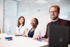 A group of three smiling people at a conference table in a modern office setting.