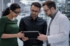Three colleagues in a laboratory are discussing data on a tablet.