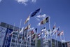 A display of various national flags in front of a modern building under a blue sky with a few clouds.
