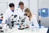 Three students are working in a laboratory, observing samples under a microscope.