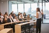 A woman gives a presentation to an audience in a modern classroom setting.