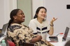 Two women are smiling and engaged in conversation at a workplace setting.