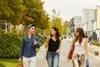 Three young adults walking and talking on a tree-lined urban street.