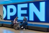 Two women are sitting on a bench in front of a large illuminated 'OPEN' sign.