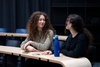 Two women with curly hair are having a conversation in a modern classroom.
