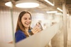 A smiling woman writes on a glass board in an office setting.