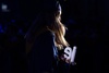 A graduate holding a decorative sign in a dimly lit ceremony.