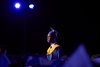 A graduate stands proudly during a graduation ceremony under purple lights.