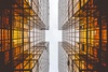 Looking upward between two symmetrical skyscrapers with a clear sky above and reflections on the glass facade.