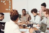 A group of six professionals engaged in a meeting around a table with laptops and documents.
