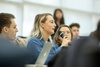 A woman holding a microphone speaks during a discussion in a classroom setting.