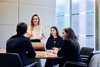 A woman is presenting to a group at a conference table in a modern office setting.