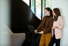 Two women are discussing and looking at a laptop in a modern office setting.