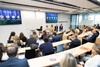 A panel discussion taking place in a modern classroom setting with attendees seated and taking notes.