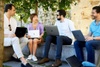 Four professionals sitting outdoors engaged in a discussion with laptops.