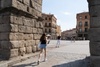 A young woman walks through an archway in a historic city square on a sunny day.