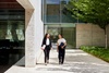 Two women walking and conversing outside a modern building.