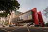 A modern architectural building with a glass facade and red accent walls situated on a city street.
