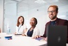 A group of three colleagues smiling and sitting at a table in a modern office.