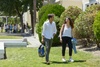A young couple walks together on a sunny day in a green park.