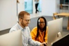 A man and a woman working together on computers in a modern office setting.