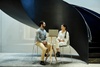 A man and a woman sitting and talking under a large, spiral staircase in a modern building.