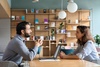 Two people are engaged in a conversation at a table with a laptop in a cozy, modern workspace.