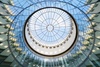 A modern glass dome structure viewed from below, showcasing a circular design and a clear sky overhead.