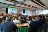 A large group of people attending a presentation in a modern classroom setting.